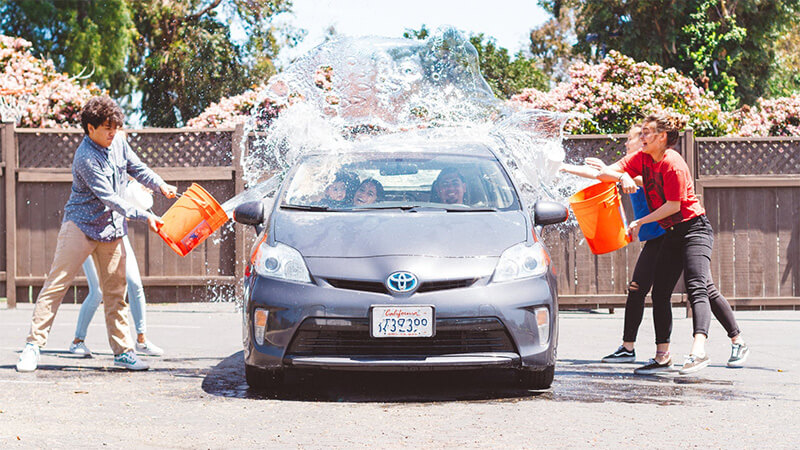 Children throw buckets of water on a Toyota Prius.