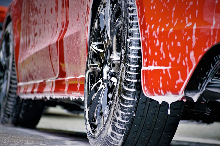 A red car drips with soap after coming out of a car wash system