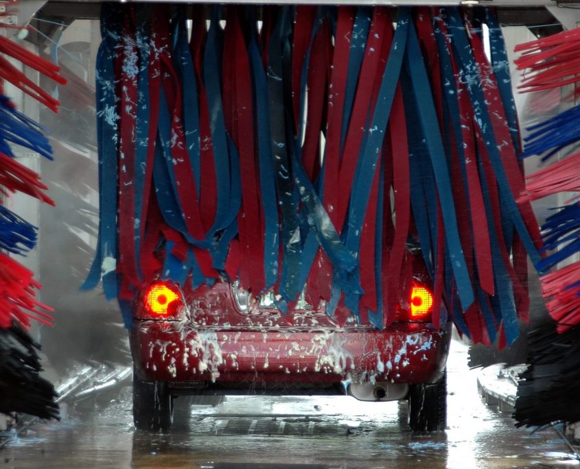 The rear end of a car disappears under a red and blue car wash curtain