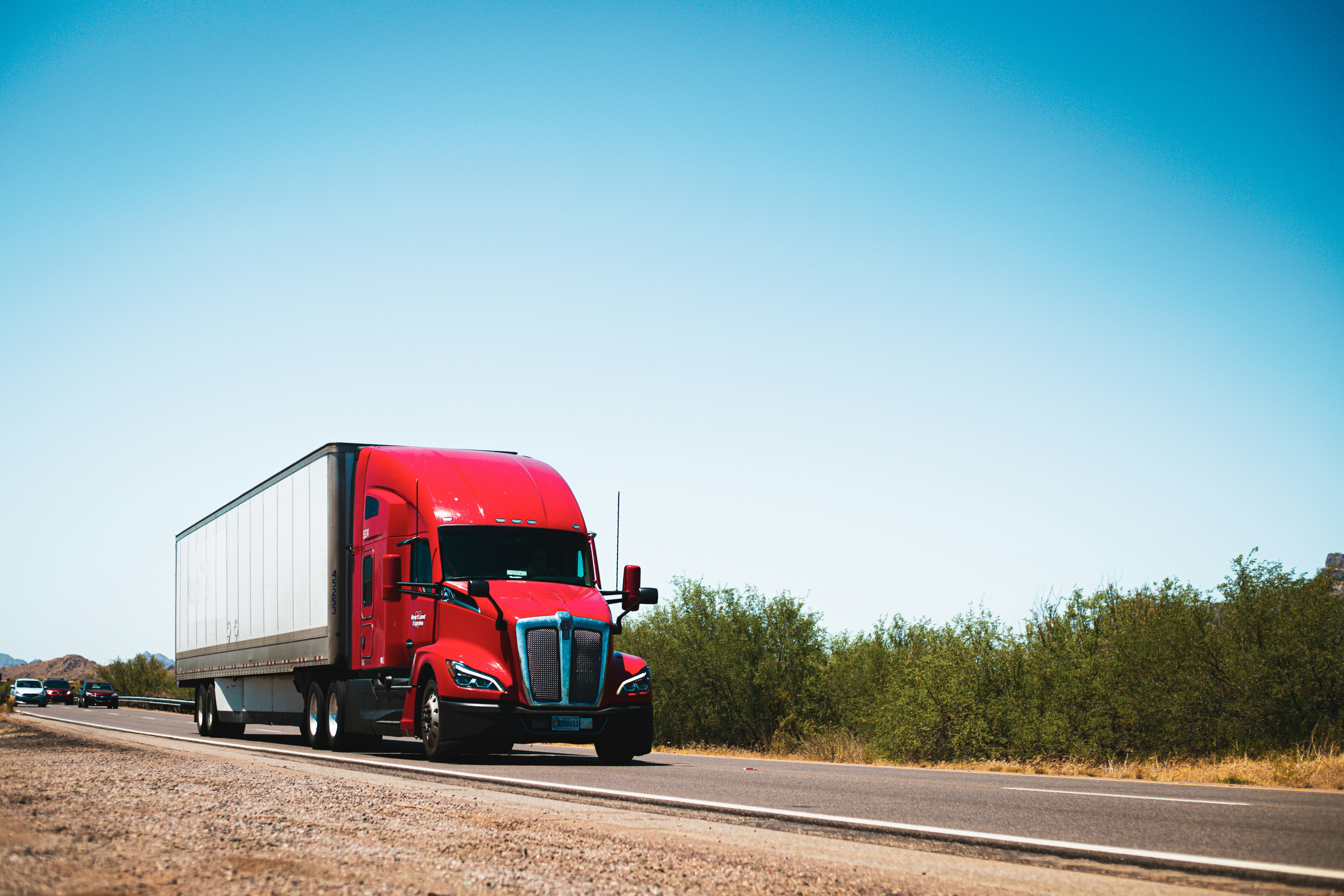 A red truck pulls a white trailer down a desert highway